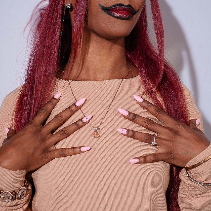 Woman with long red hair and makeup posing with hands on chest against a plain background