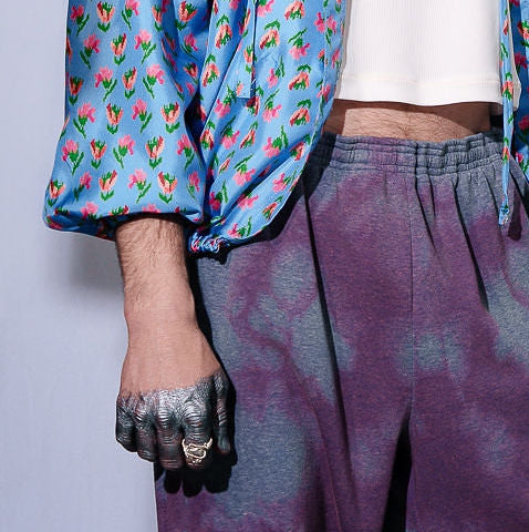 Person wearing a colorful jacket and tie-dye pants against a plain background