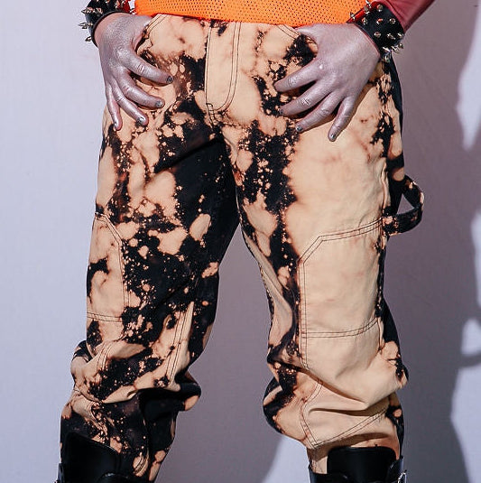 Person wearing an orange sleeveless top and beige pants with black accents on a plain background