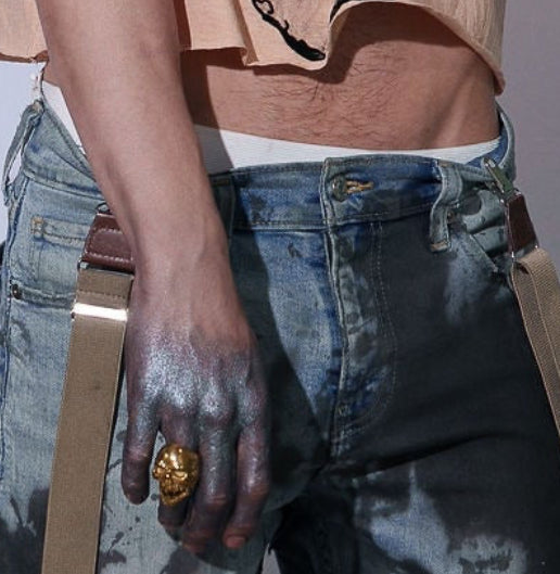 Person wearing a beige t-shirt with a graphic design and blue jeans against a light gray background