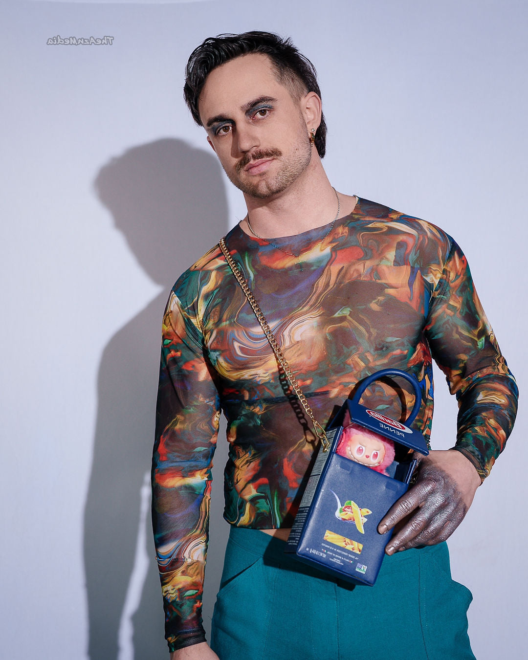 Person wearing a colorful long-sleeve shirt holding a blue bag with a red item against a plain background