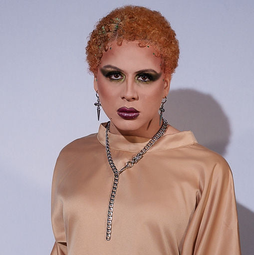 Person wearing a beige long-sleeve top with a high collar against a light gray background