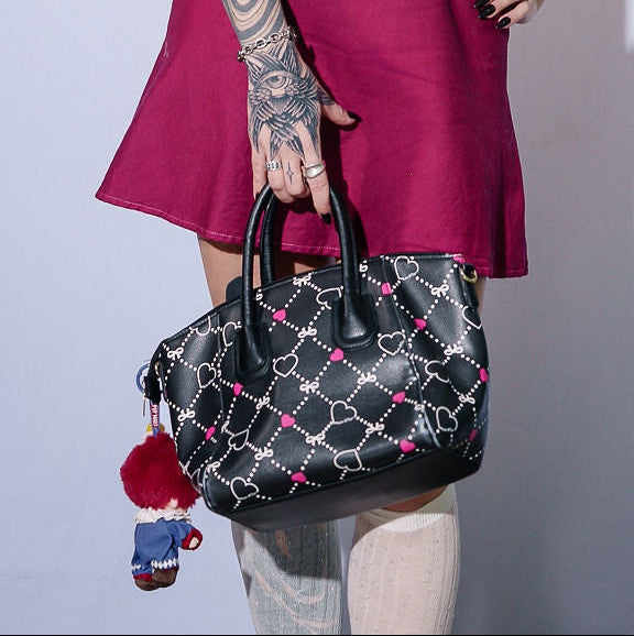 Woman in a red dress with tattoos holding a black handbag against a white background