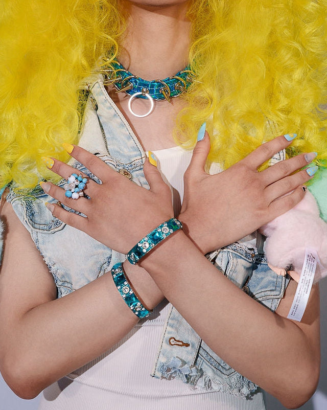 Person with bright yellow wig and colorful makeup holding plush toys against a plain background