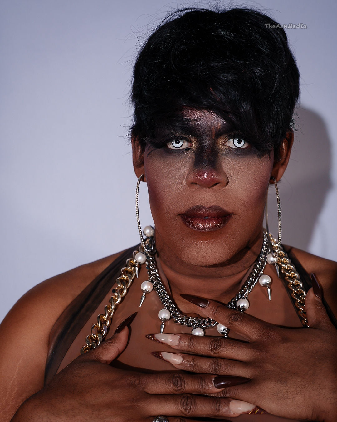 Person with dark makeup and jewelry against a plain background